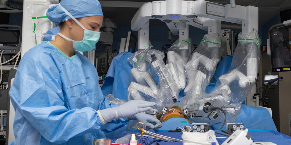 A member of a surgical care team attends the site of a surgical procedure being performed with a robotic surgical system, controlled remotely by a surgeon at a console.