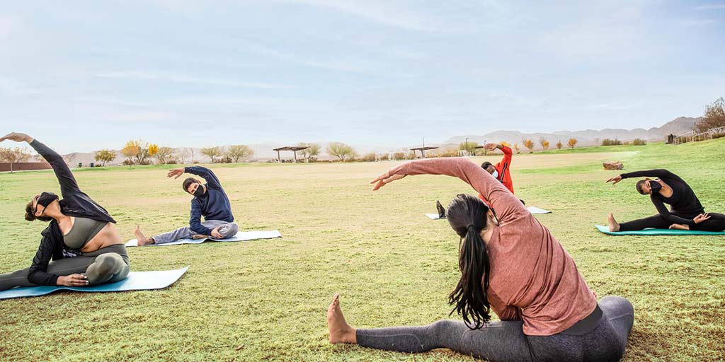 A group of people social distancing and wearing masks while practicing yoga outside in a field during the Covid-19 pandemic.