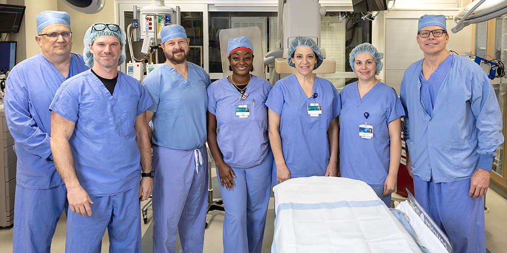 Seven people gathered for a group photo in a patient exam and procedure room.