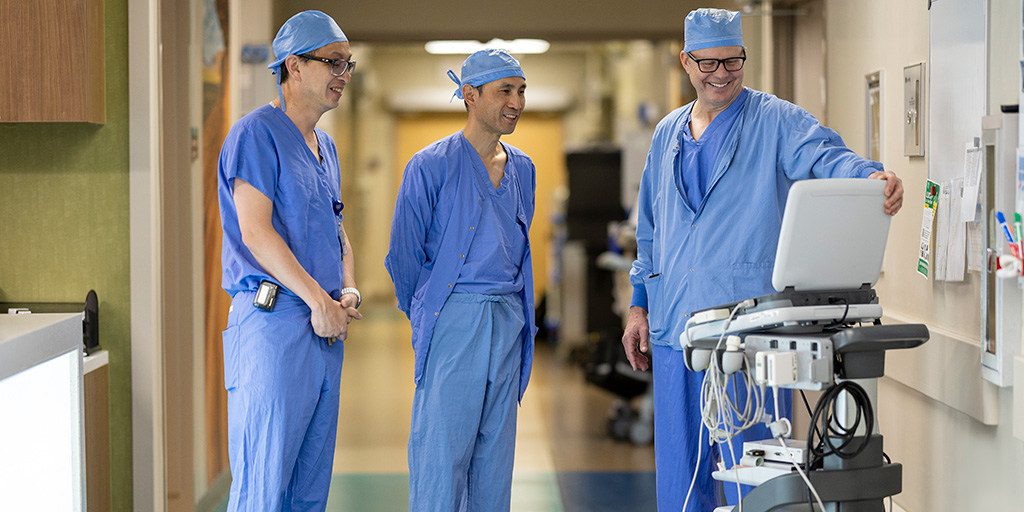 Three people stood in a hallway and had a discussion while looking at a monitor device.